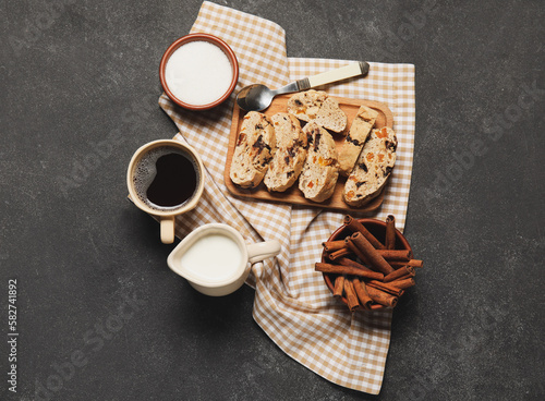Board with delicious biscotti cookies, cup of coffee and cinnamon on black grunge background