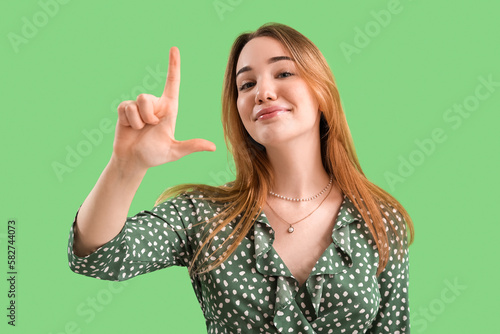 Bilde på lerret Young woman showing loser gesture on green background
