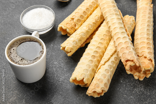 Delicious wafer rolls, sugar and cup of coffee on black grunge background