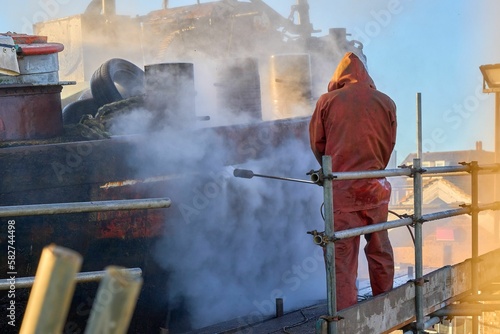 Workman pressure washing the hull of a boat