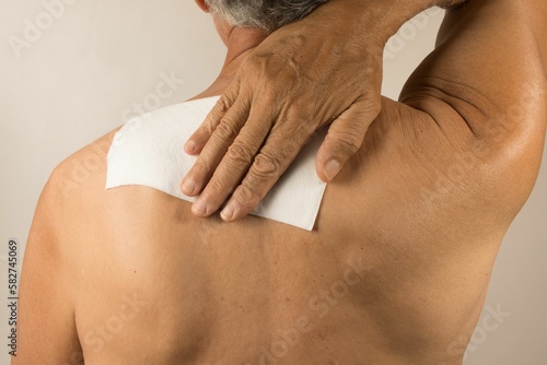 Man wearing a medicated patch for pain relief near his shoulder blade and upper back.