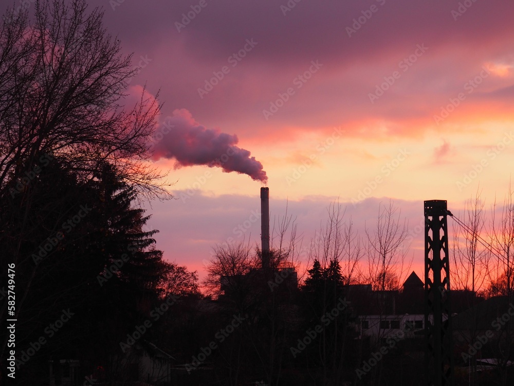 Silhouette of industrial chimneys with smoke at sunset