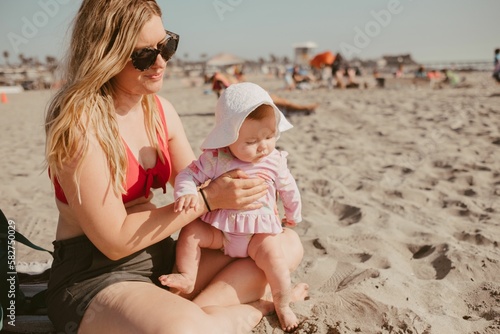 Closeup shot of a mother and a baby playing in sand on the beach © Aubrey Westlund/Wirestock Creators