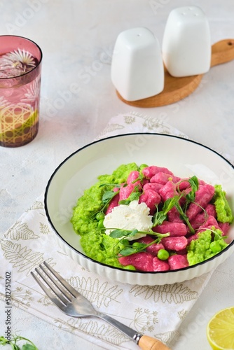 Beetroot dumplings or gnocchi with mashed green peas and curd cheese in a white plate on a light concrete background. Vegetarian recipes, beets.