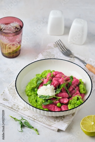 Beetroot dumplings or gnocchi with mashed green peas and curd cheese in a white plate on a light concrete background. Vegetarian recipes, beets.