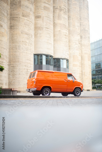 Orange 70   s boogie van rear 3 4 view portrait  with tall concrete backdrop