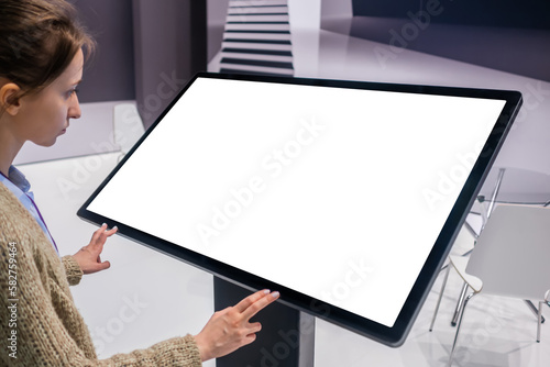 White screen, mock up, future, copyspace, template, technology concept. Woman looking at blank interactive touchscreen white display of electronic kiosk at futuristic exhibition or museum photo