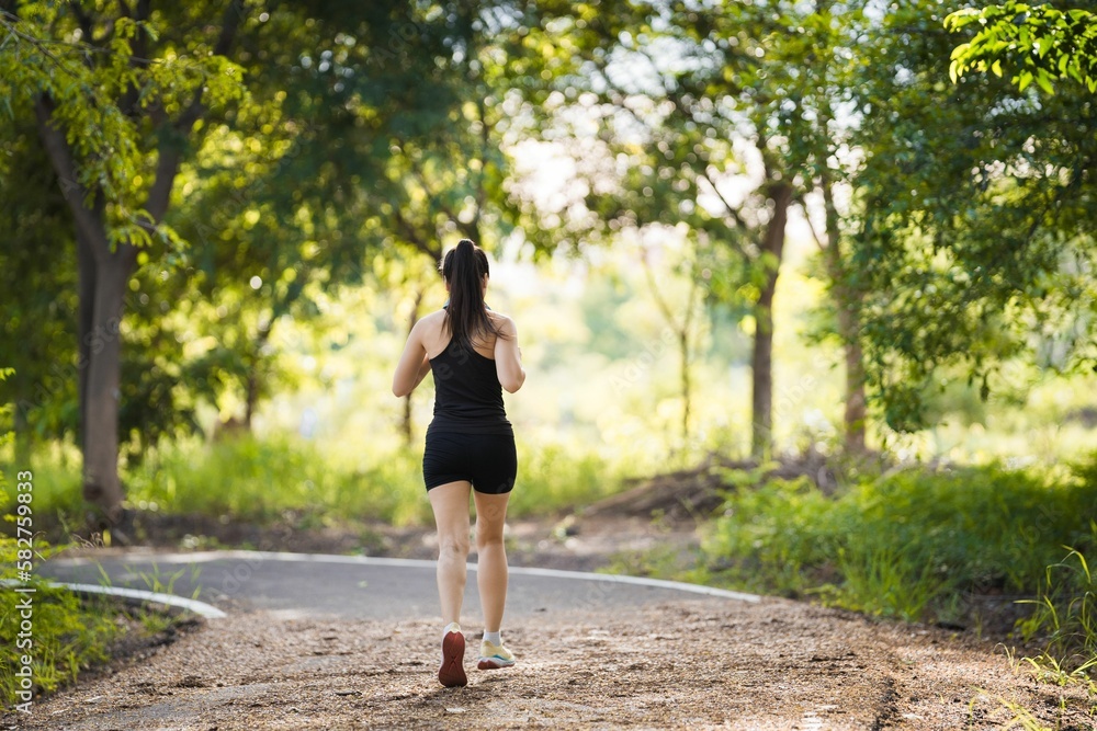 Female jogging in a park in black sportswear surrounded by greenery