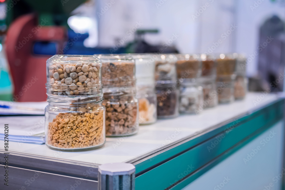 Different kinds of pelleted compound feed, fodder in glass jars: before and after extrusion - food for domestic animals at agricultural exhibition, trade show: close up. Agriculture, husbandry concept Different kinds of pelleted compound feed, fodder in glass jars: before and after extrusion - food for domestic animals at agricultural exhibition, trade show: close up. Agriculture, husbandry concept
