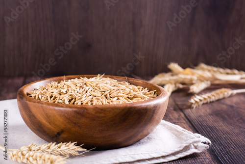 Oat seeds in a wooden bowl and ears on the table. Organic harvest.