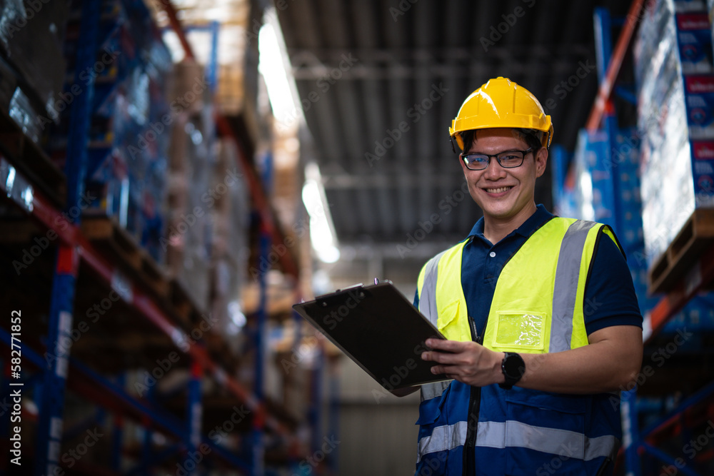 Asian male worker wearing Hard Hat with clipboard Checks Stock and Inventory in the Retail Warehouse. Asian male worker wearing Hard Hat with clipboard Checks Stock and Inventory in the Retail Warehouse.