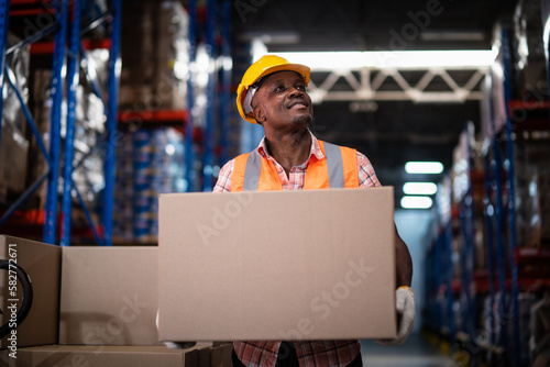 African American male warehouse worker hold cardboard box packaging in warehouse distribution center environment.