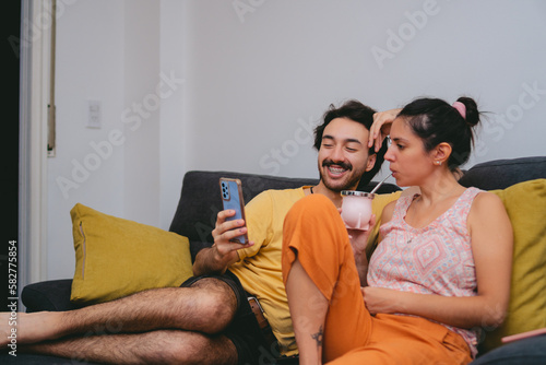 Young Argentine friends drinking mate while looking at their cell phone on the sofa at home. Copy space. photo