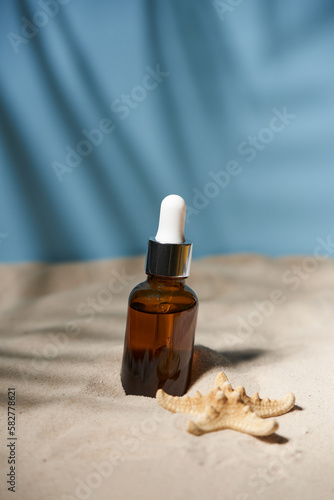 Summer sunscreen essence on sand background with seashells and starfish.