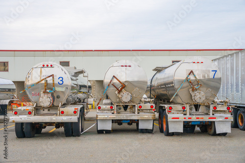 Row of three shiny metal tanker trucks used to transport fuel.