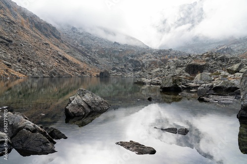 Scenic shot of a small lake surrounded by rocks in the Alps on a foggy day