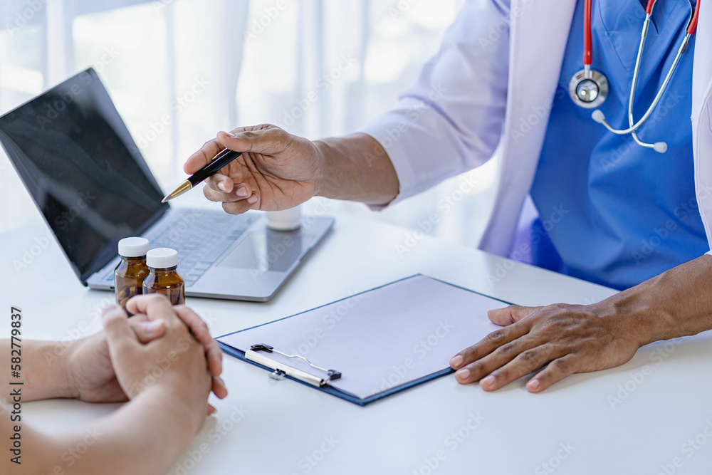 Obraz premium Doctor and patient giving consultation and diagnosis sitting together At table near window in hospital medicine concept with pill bottle and prescription sheet with laptop beside