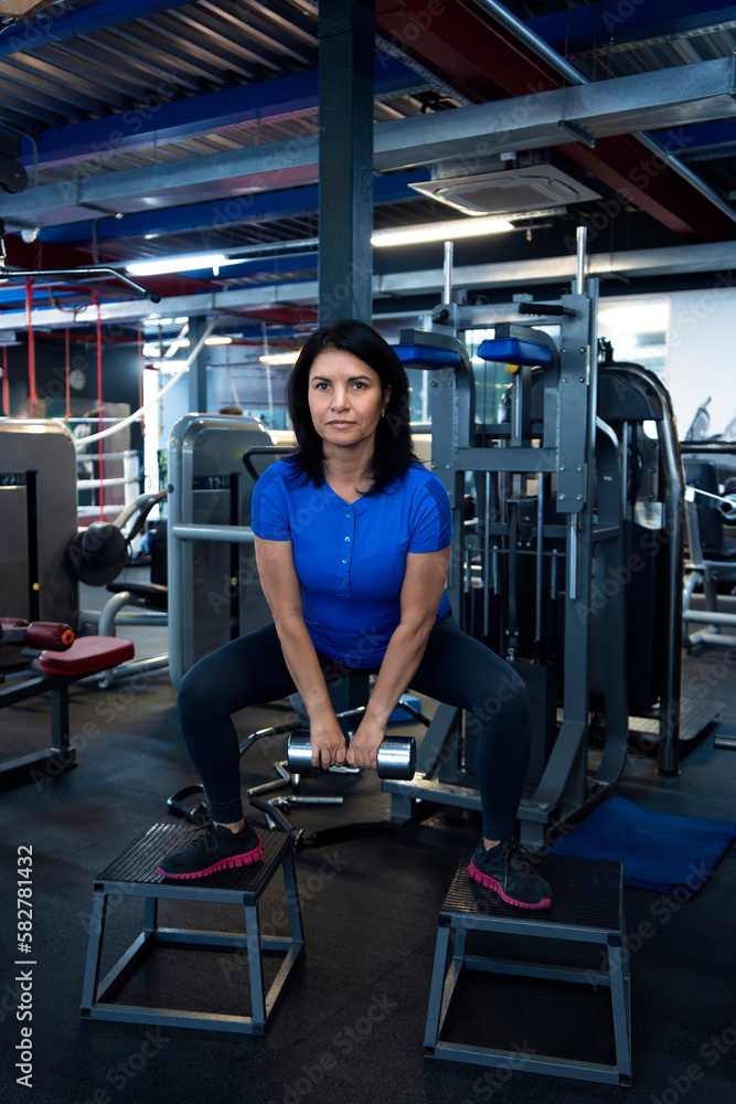 A woman doing physical exercise with dumbbell in the gym. Lower body workout. Sport and fitness. A woman doing physical exercise with dumbbell in the gym. Lower body workout. Sport and fitness.