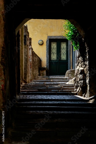 Vertical shot of a narrow walkway tunnel with stairs leading to a door in Argegno Italy photo