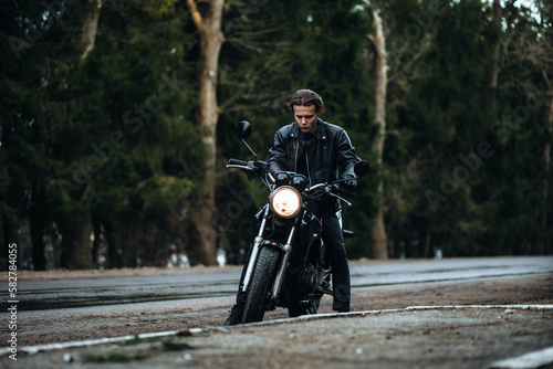 male motorcyclist in a leather jacket sits on a retro motorcycle on a forest road.