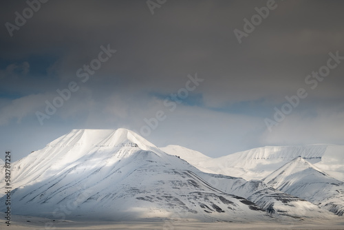 2022-05-09 SNOW COVERED MOUNTAIN PEAKS WITH A DARKENING SKY NEAR SVALBARD NORWAY IN THE ARCTIC