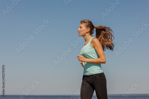 Fototapeta Naklejka Na Ścianę i Meble -  jogging, sporty woman runs in morning on seashore. fitness millennial female trains for marathon, healthy lifestyle, love for her body, mental and physical condition, sportswear, champion