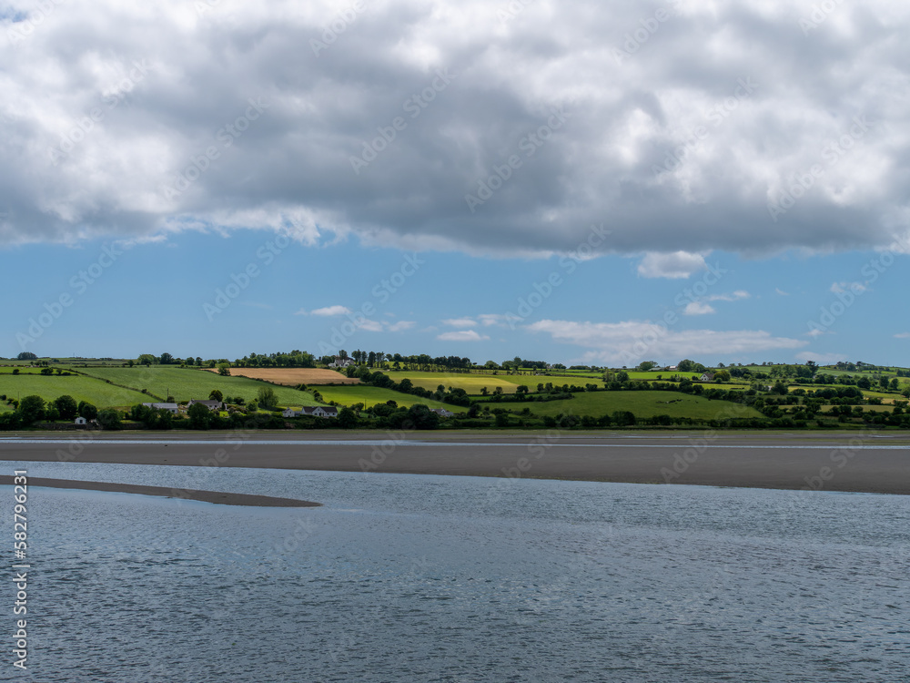 White cumulus clouds in the sky over the hilly Irish countryside. Green hills on a nice summer day. Irish countryside, County Cork. Green grass field near body of water, white clouds