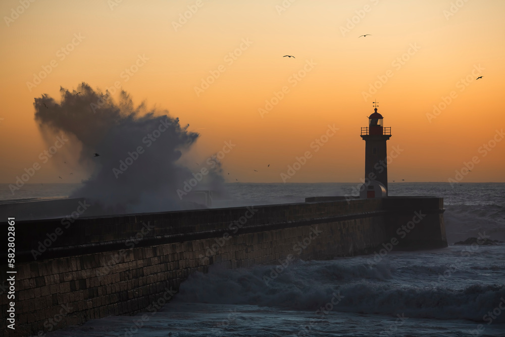 Big wave at the lighthouse against the background of the sunset. Atlantic, Portugal.