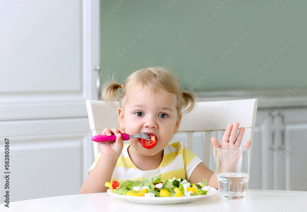 Little caucasian toddler have meal.Funny cute girl stitting at table and eating fresh vegetables salad. Little caucasian toddler have meal.Funny cute girl stitting at table and eating fresh vegetables salad.