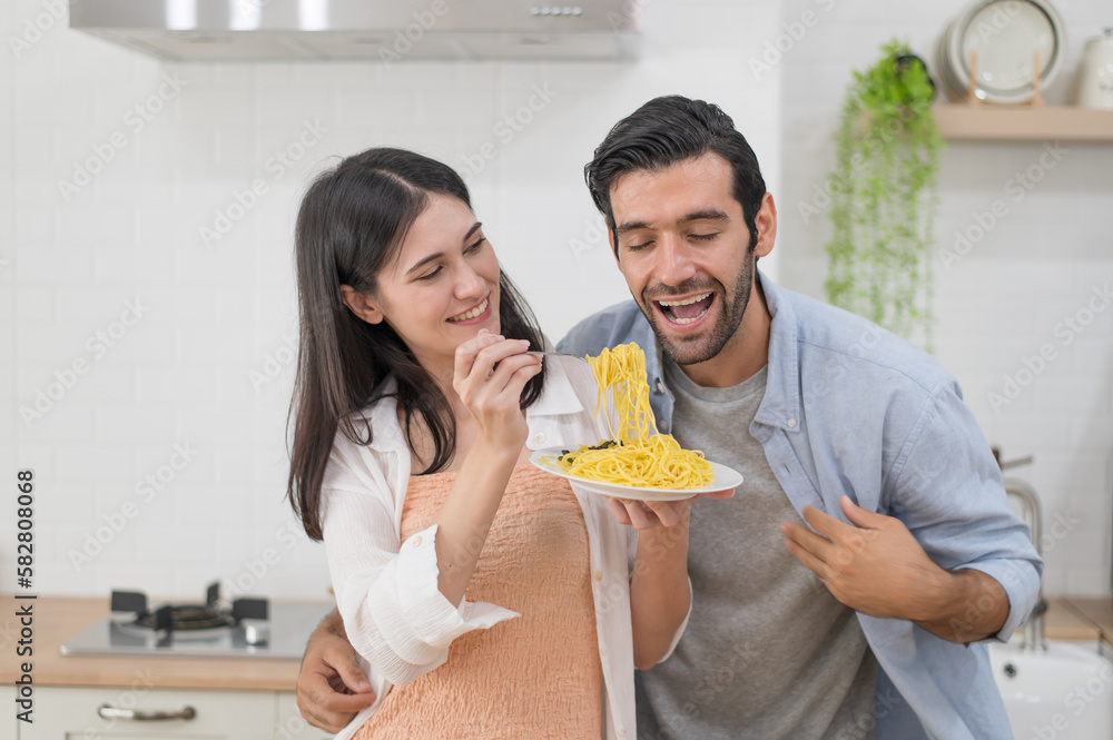 Happy young couple cooking together in the kitchen, feeding each other in their kitchen at home Happy young couple cooking together in the kitchen, feeding each other in their kitchen at home