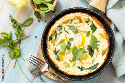 Healthy frittata or stuffed omelette in pan on rustic wooden background. Italian omelette with organic spinach and bell pepper. View from above.