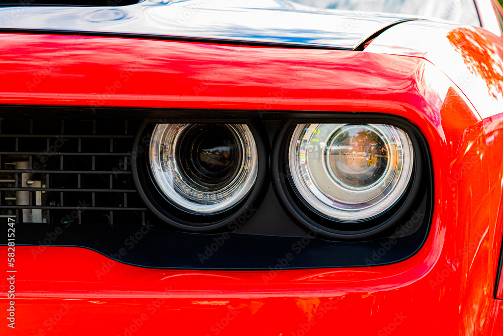Close up of headlight detail of modern luxury sportscar with reflection on red paint. Front view of supercar. Concept of car detailing and paint protection background. Close up of headlight detail of modern luxury sportscar with reflection on red paint. Front view of supercar. Concept of car detailing and paint protection background.