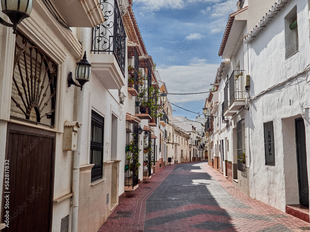 Nerja, Spain - October 9, 2021: Typical Andalusian street with whitewashed houses in a sunny day.  Nerja, beautiful touristic village in Costa del Sol. Malaga province, Andausia, Spain, Europe
