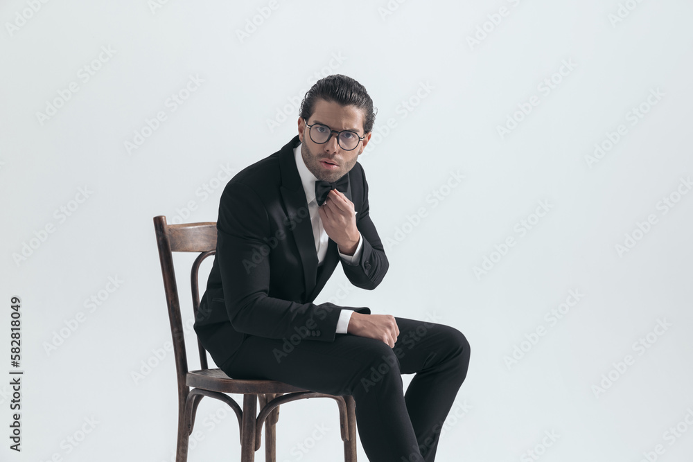 side view of cool elegant man with glasses sitting and adjusting bowtie side view of cool elegant man with glasses sitting and adjusting bowtie
