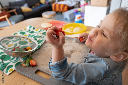 2 year old learns to cut and prepare fruit and veggies to work on picky eating habits; child eats strawberry photo