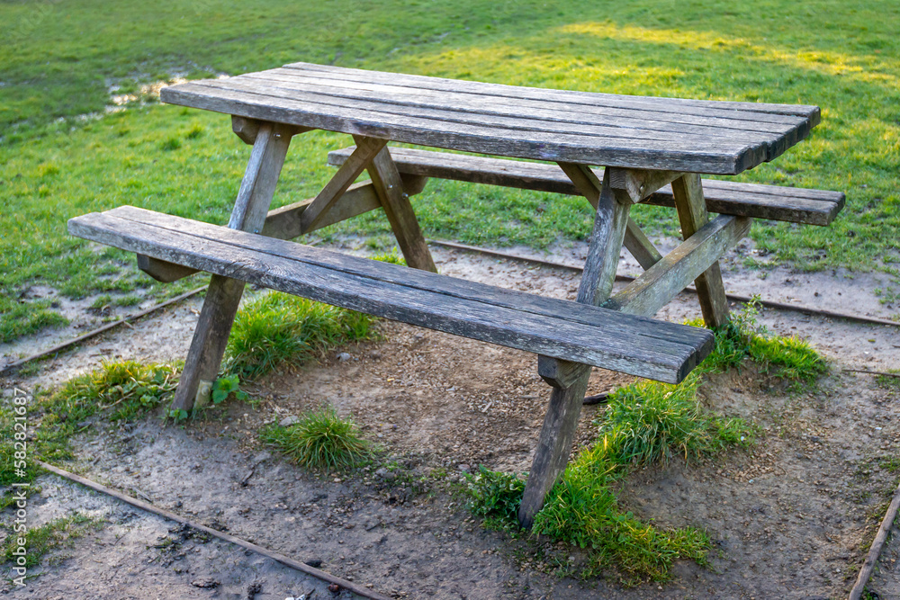 Old rustic wooden picnic table in outdoor park picnic area with green grass and gravel underneath. 