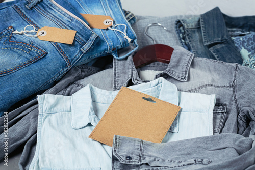 Sustainable still life with Stack of blue jeans and denim shirts on hanger and empty craft card. Second hand apparel idea. Circular fashion, donation, charity concept photo