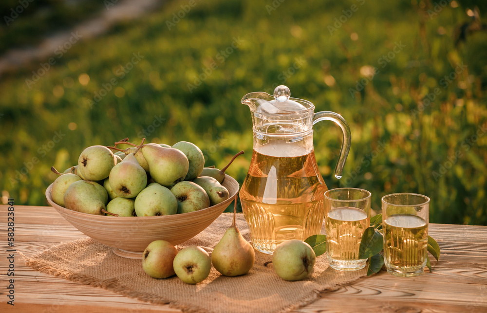 Two glasses with pear juice and basket with pears on wooden table with natural orchard background on sunset light. Vegetarian fruit composition Two glasses with pear juice and basket with pears on wooden table with natural orchard background on sunset light. Vegetarian fruit composition