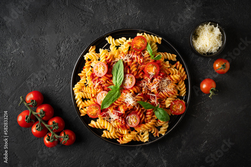 Fusilli pasta with tomatoes, basil, parmesan, and sauce on back background
