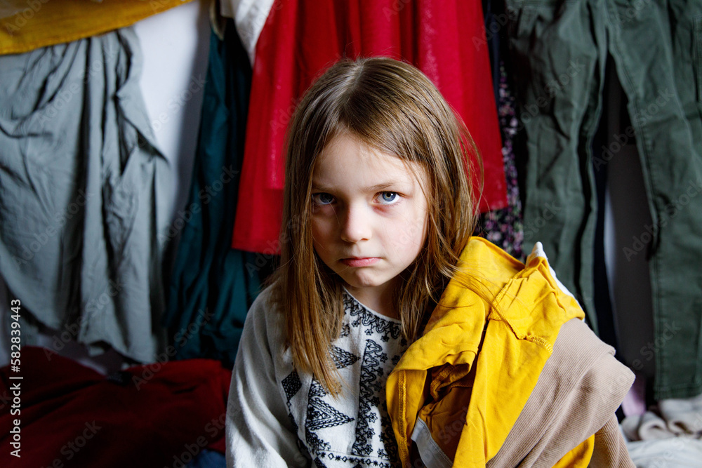 Dziewczynka zero waste - eko - era konsumpcjonizmu - za dużo ubrań, niezadowolone dziecko - smutne dziecko - nie wie, w co się ubrać - obrazy, fototapety, plakaty 