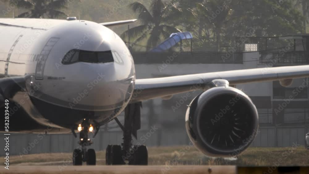 Close up, wide body airliner taxiing at Phuket Airport. Airliner in backlight. Airplane on the taxiway, palm trees in the background Close up, wide body airliner taxiing at Phuket Airport. Airliner in backlight. Airplane on the taxiway, palm trees in the background