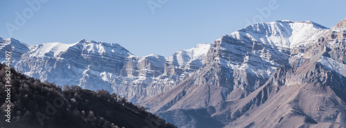 Panorama of a mountain range from layers of rocks with the first snow on the rocks and slopes, autumn mountains with the first snow