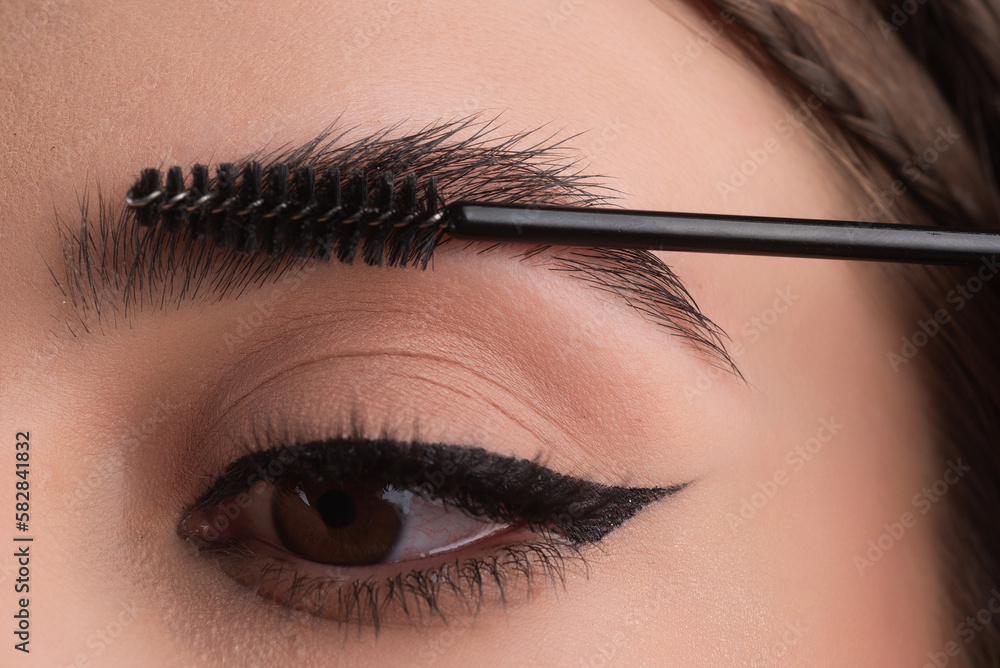 Naklejka premium Closeup eyebrows with eyebrow brush. Close up brows, eyebrows lamination. Brow procedures. Long eyelashes, eyebrows, macro.
