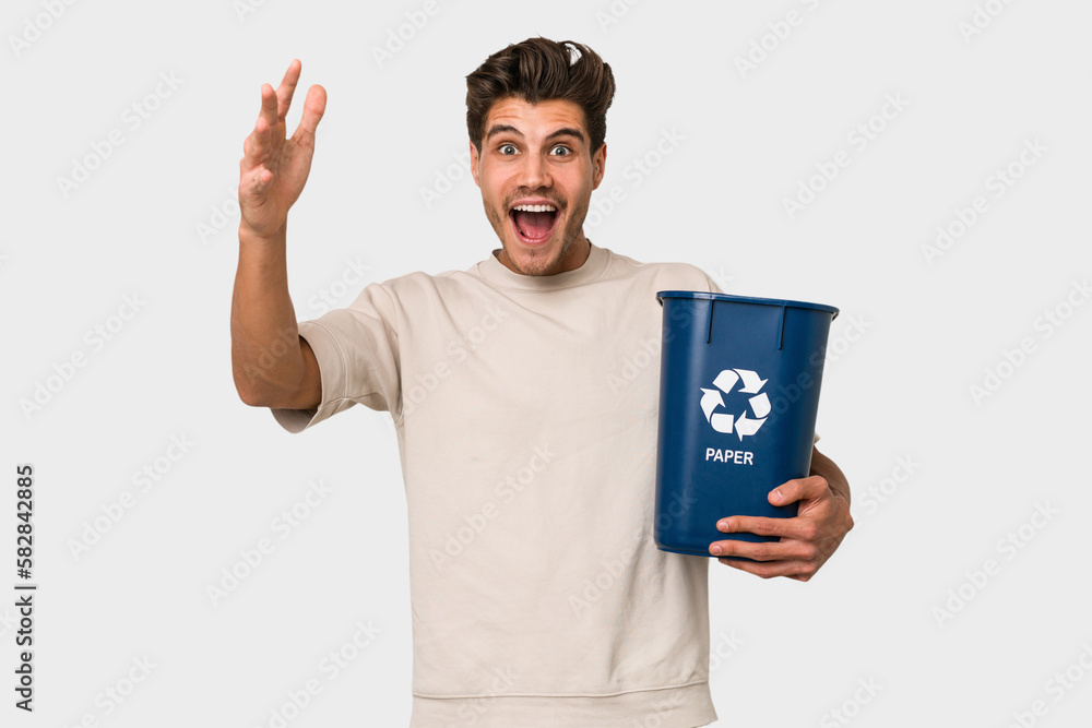 Young caucasian man holding a paper trash for recycle receiving a pleasant surprise, excited and raising hands. Young caucasian man holding a paper trash for recycle receiving a pleasant surprise, excited and raising hands.