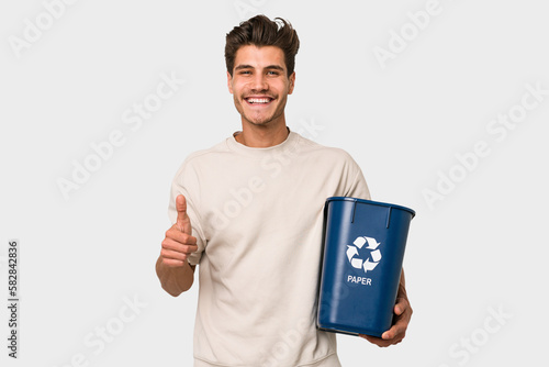 Young caucasian man holding a paper trash for recycle smiling and raising thumb up