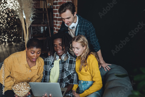 Diverse group of college students  friends  young people watching movies or cinema together on laptop  have fun  eating popcorn. Concept of international friendship  leisure time  home activity