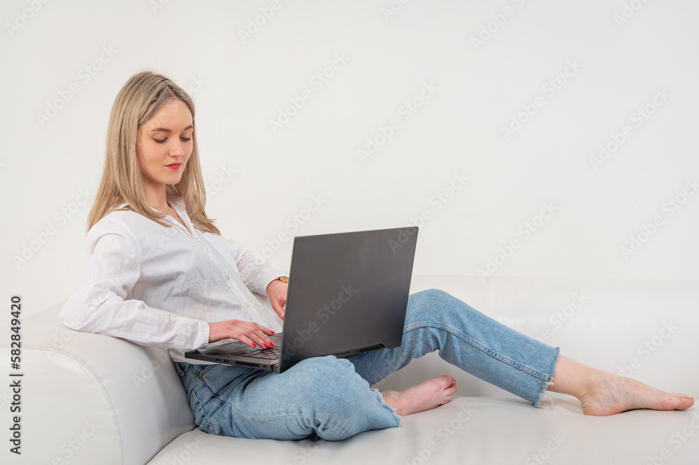 young emotional girl sitting on laptop on sofa, isolated on light background girl shopping or chatting online in social networks, remote work. A place for writing young emotional girl sitting on laptop on sofa, isolated on light background girl shopping or chatting online in social networks, remote work. A place for writing