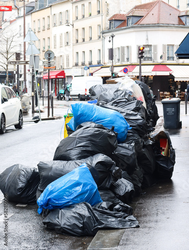 Pile of garbage bags full with rubbish at sidewalk with Paris buildings, urban scene in background. It’s relating to garbage collectors, cleaning agent and wage labor strike against the pension reform