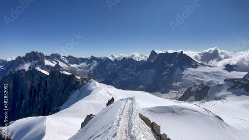 Сlimber walking narrow path on mountain ridge under Aiguille du Midi 3842m with French Alps mountains peaks panorama. Beauty of Nature and extreme people activity concept