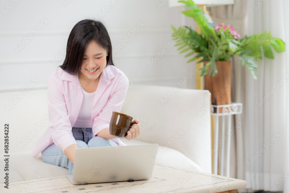 Young asian business woman work from home with laptop computer and drinking coffee on sofa in living room, freelance girl using notebook sitting on couch with comfort and relax, lifestyles concept. Young asian business woman work from home with laptop computer and drinking coffee on sofa in living room, freelance girl using notebook sitting on couch with comfort and relax, lifestyles concept.